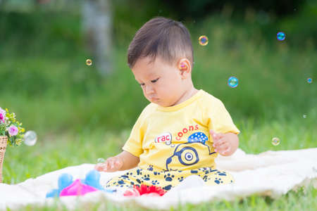 Asia Baby boy sitting on green grass in the park with soap bubblesの写真素材