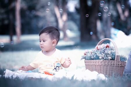Asia Baby boy sitting on green grass in the park with soap bubbles