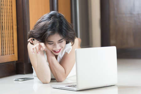 happy asia woman lying on floor with the laptop at homeの写真素材