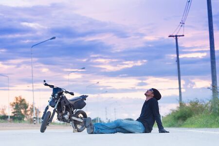 Biker relax sitting with motorbike on country road in sunsetの写真素材