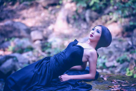 High fashion shot of asia elegant woman in black long dress lying on stoneの写真素材