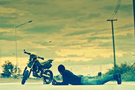 Biker relax lying with motorbike on country road in sunset, cross process effect