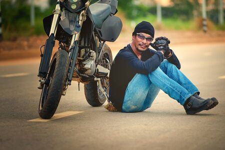 Biker relax sitting with motorbike on country road in sunsetの写真素材