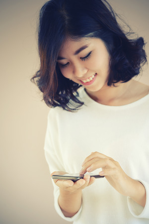 asia Young beautiful woman writes SMS to mobile phone, technology conceptの写真素材