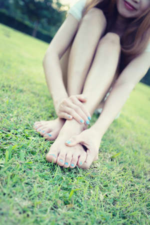 relaxation concept, relaxed young woman with bare feet sitting on grass, focus foot, vintage effectの写真素材