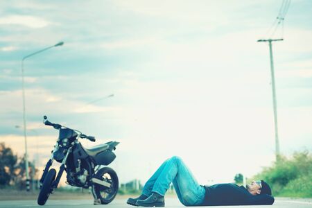 Biker relax lying with motorbike on country road in sunsetの写真素材
