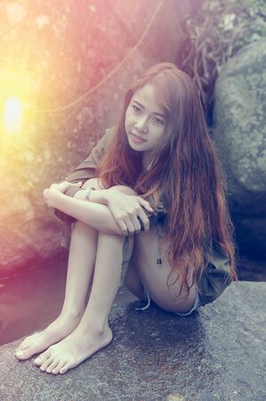 Asia Beautiful young girl sitting on the stone in water fallの写真素材