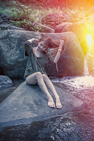 Asia Beautiful young girl sitting on the stone in water fall, add flare for mood and tone styleの写真素材