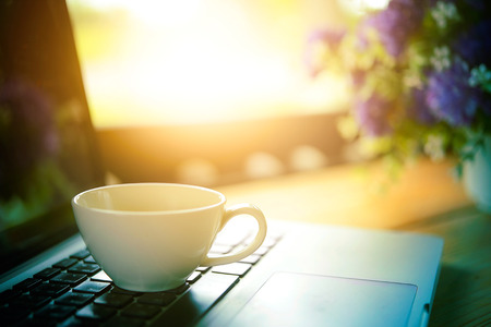 white Cup of coffee and laptop on wooden table. business concept, add flare effect