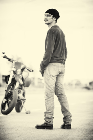 portrait of man biker standing on road with motorcycle in sunset, vintage styleの写真素材