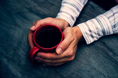 woman hands holding a cup of coffee over wooden table, top viewの写真素材