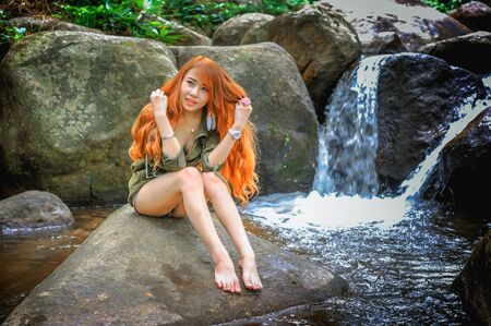Asia Beautiful young girl sitting on the stone in water fallの写真素材