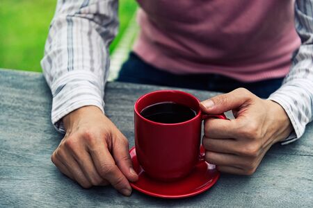 woman holding hot cup of coffee on wood tableの写真素材