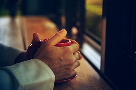 woman hand holding a red cup of coffee on wooden tableの写真素材
