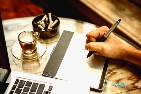 hand of Graphic Designer working with interactive pen display with coffee glass and ashtrayの写真素材
