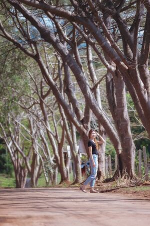 Beautiful asia woman in black t shirt and jeans stand on the road under tunnel tree in the sunny day,bright sunlightの写真素材