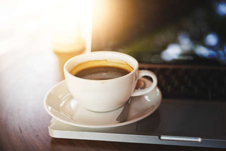 Cup of coffee and laptop on wooden table in morningの写真素材