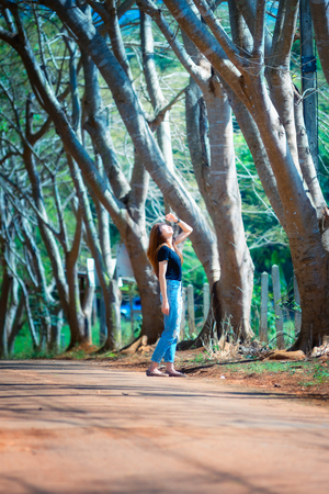 Beautiful asia woman in black t shirt and jeans stand on the road under tunnel tree in the sunny day,bright sunlightの写真素材
