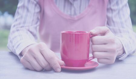 woman holding hot cup of coffee on wood tableの写真素材