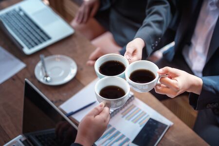 young business people holding cups of coffee while having coffee break in officeの写真素材