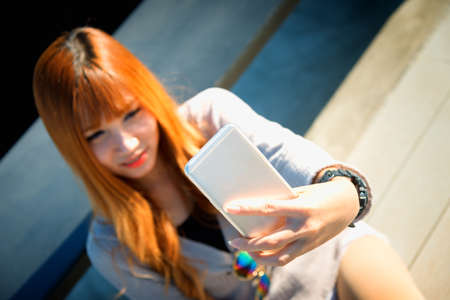 asia woman sitting against bench on floor and selfie on smart phone on sun