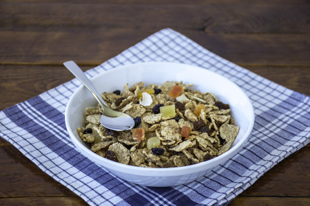 A bowl full of muesli cereals with spoon over a wooden tableの写真素材