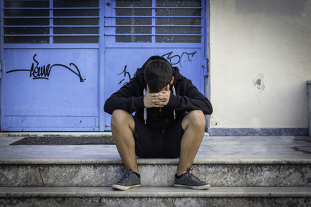 Little boy sad sitting alone at school hides his face