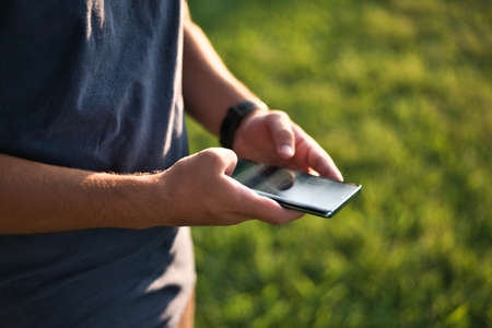 Teenage Boy Using Phone In Urban Setting, Sitting on Grass at sunsetの写真素材