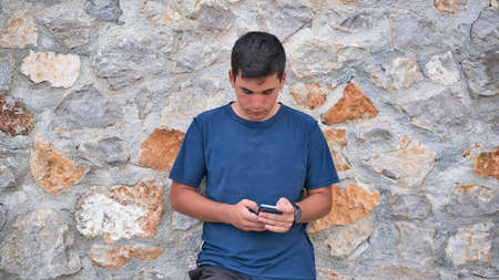 Teenage Boy Using Phone In Urban Setting, Sitting on Grass at sunsetの写真素材