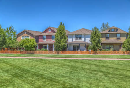 Neighborhood park with green grass and row of homesの写真素材