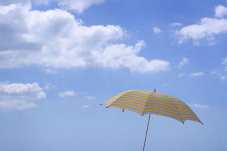 Yellow Striped Umbrella against a Blue Sky with Cloudsの写真素材