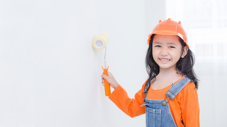 Smile cute asian little girl holding paint roller with copy space in the white roomの写真素材