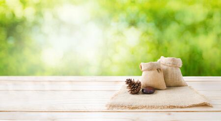 Two of blank hemp sack bag and pine cones on wood table top floor over blur green bokeh background with copy spaceの写真素材