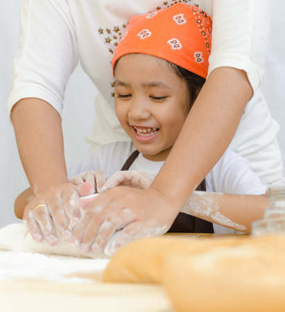 Close up shot of Asian little girl with hands of mother kneading the dough for making the bakery on...