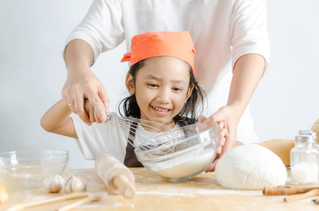 Close up shot Asian little girl holding stainless steel whisk and bakery dough flour in glass bowl and mother hands, shallow depth of fieldの写真素材