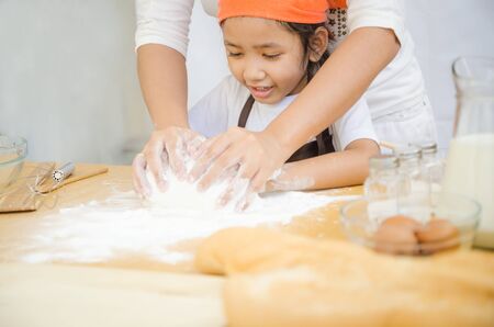 Close up shot of Asian little girl with hands of mother kneading the dough for making the bakery on...