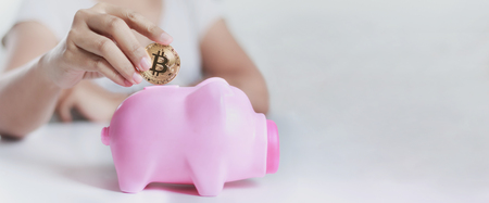 Close up shot hands of woman putting gold bitcoin to pink piggy bank, With copy space for banner design, Shallow depth of field, Select focus on handの写真素材