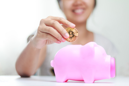 Close up shot Happy smile woman putting gold bitcoin to pink piggy bank, Shallow depth of field, Select focus on handの写真素材