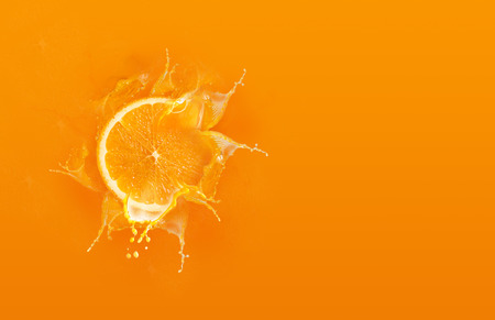 Slide cut piece of orange drop on orange background with orange juice splash water with copy spaceの写真素材