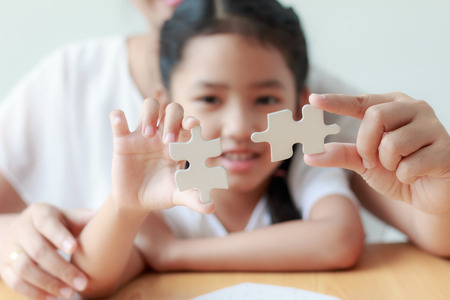 Asian little girl playing jigsaw puzzle with her mother for family concept shallow depth of field select focus on handsの写真素材