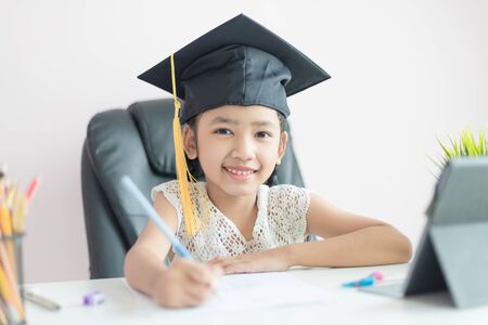 Little Asian girl wearing graduate hat doing homework and smile with happiness for success of education concept select focus shallow depth of fieldの写真素材