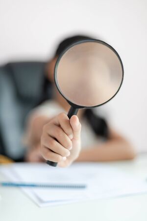 Little Asian girl using magnifier doing homework and smile with happiness for education concept select focus shallow depth of fieldの写真素材