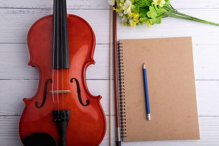 Close-up shot violin orchestra instrumental and notebook over white wooden background select focus...