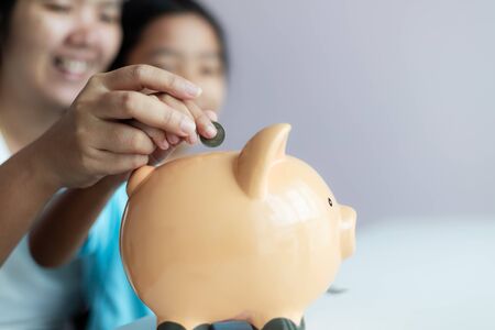 Mother and daughter putting coin into the piggy bank for money saving for the future concept select focus shallow depth of fieldの写真素材
