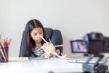 Little Asian girl crafting wooden model and live streaming for social media with happiness by camera select focus shallow depth of fieldの写真素材