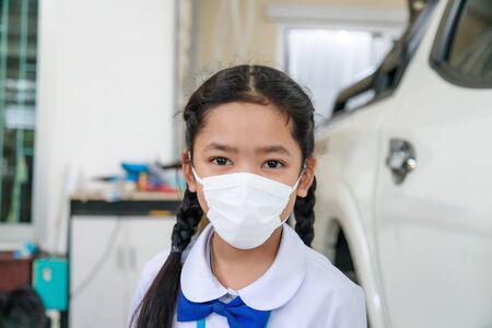 Little Asian girl in Thai student uniform wearing virus protective flu mask, Health care concept, select focus shallow depth of fieldの写真素材
