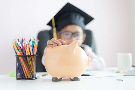 Little Asian girl putting the coin into piggy bank and smile with happiness for money saving to wealthness in the future of education concept select focus shallow depth of fieldの写真素材