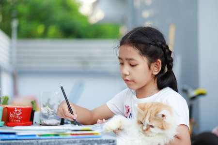 Portrait of a Little Asian girl doing homework and hugging her Persian cat with happiness, select focus shallow depth of fieldの写真素材