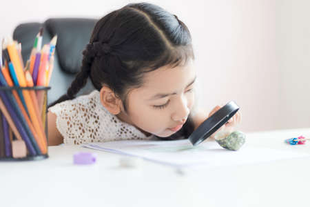 Little Asian girl using magnifier doing homework for education concept select focus shallow depth of fieldの写真素材
