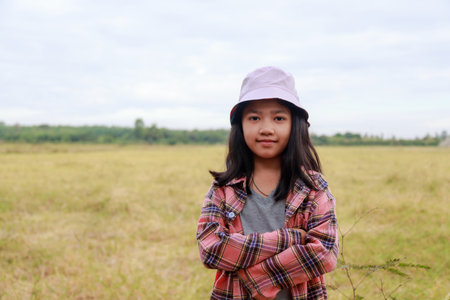 The little Asian girl Stands confidently with her arms crossed at the tropical farm field, little farmer smile with happinessの写真素材